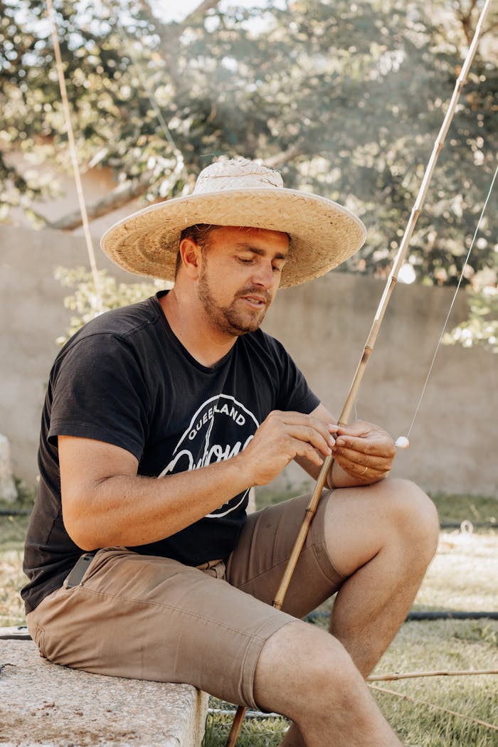 Man wearing straw hat preparing fishing rod in a São Paulo garden.