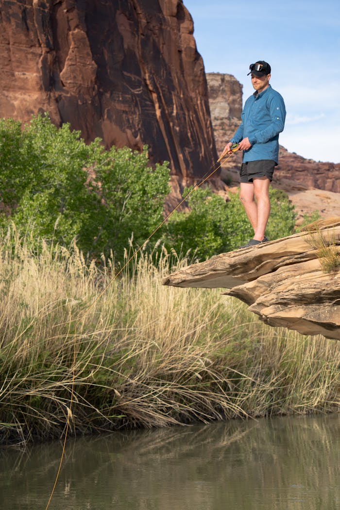 Adult man fishing from a rocky cliff in a scenic rural area of Castle Dale, Utah during daytime.
