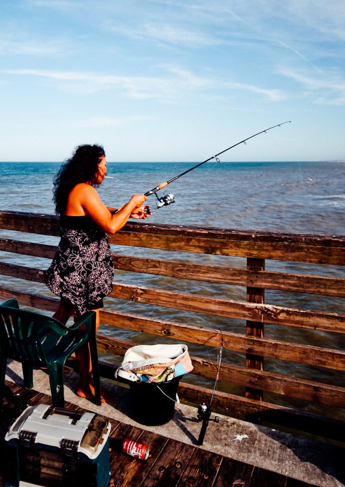 Woman fishing with rod from a wooden pier overlooking the sea in Jacksonville, FL on a sunny day.